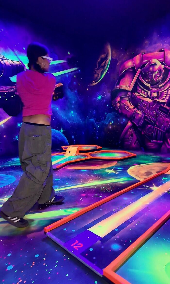 Person spielt Schwarzlicht-Minigolf mit Weltraumdesign bei Battlekart Dissen