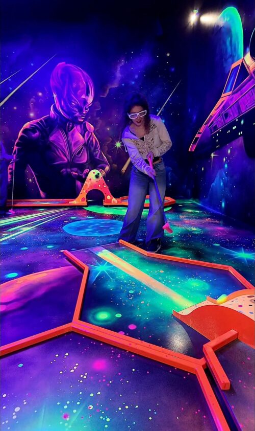 Person spielt Schwarzlicht-Minigolf mit Sci-Fi-Motiven bei Battlekart Dissen