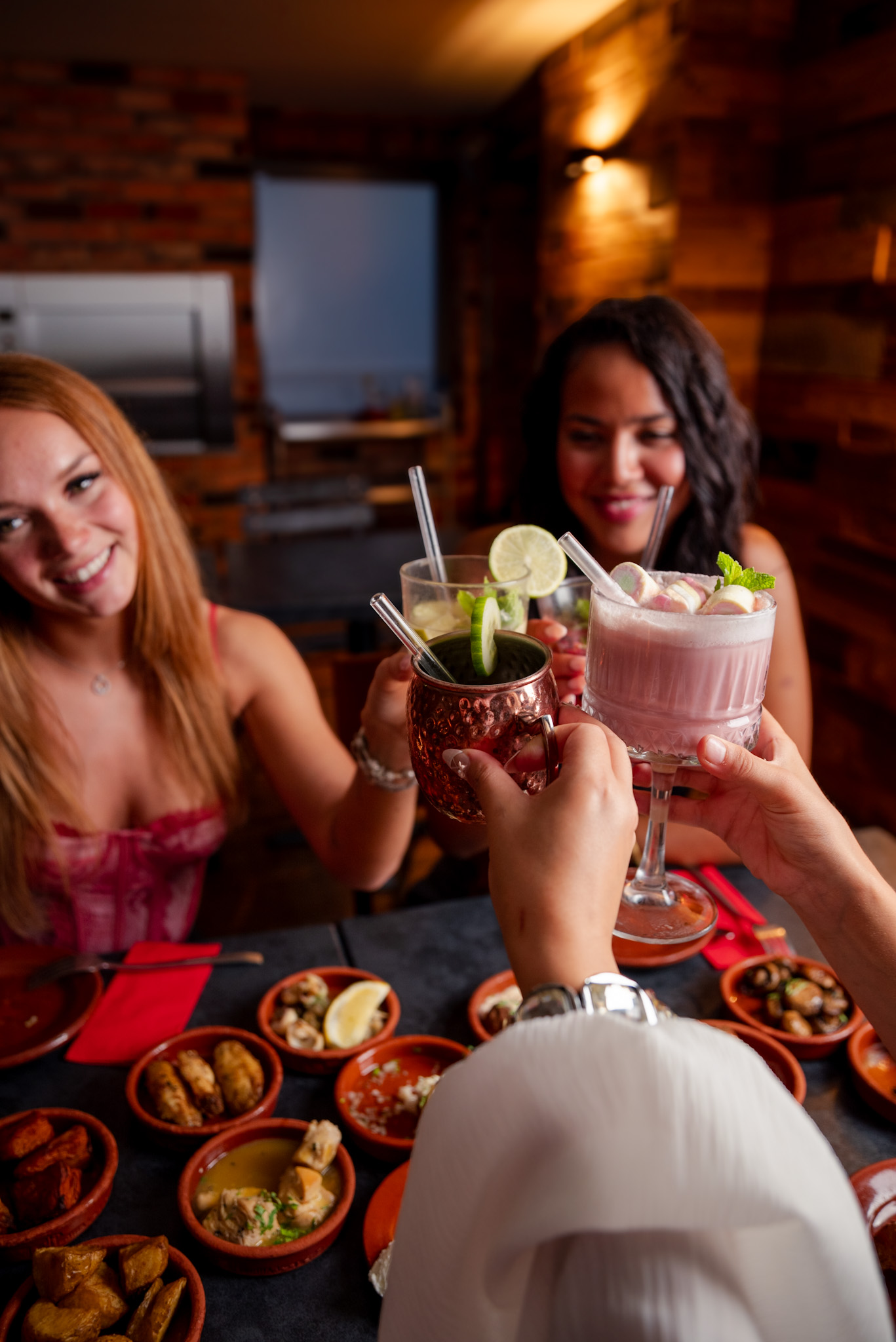 Freundinnen stoßen mit Cocktails im Tapas & More Dortmund an, umgeben von Tapas auf dem Tisch.