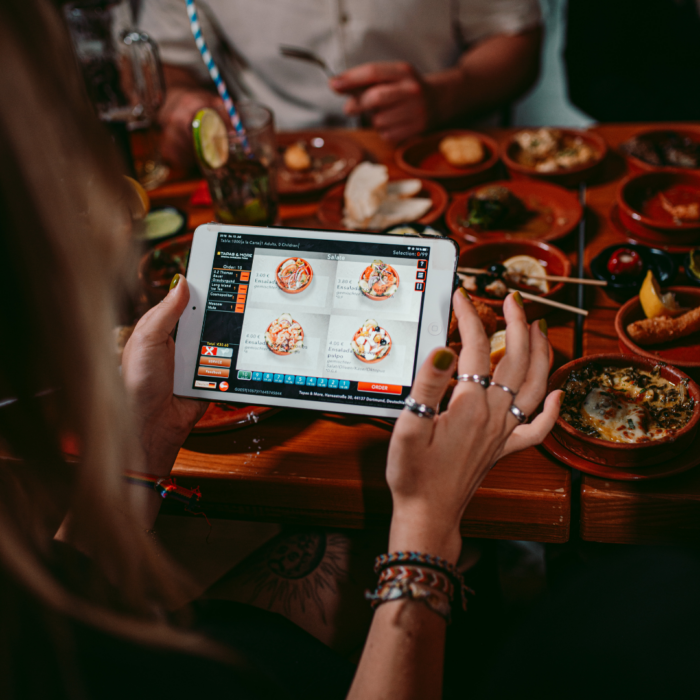 Gast bestellt Tapas über ein Tablet an einem voll gedeckten Tisch bei Tapas & More Dortmund