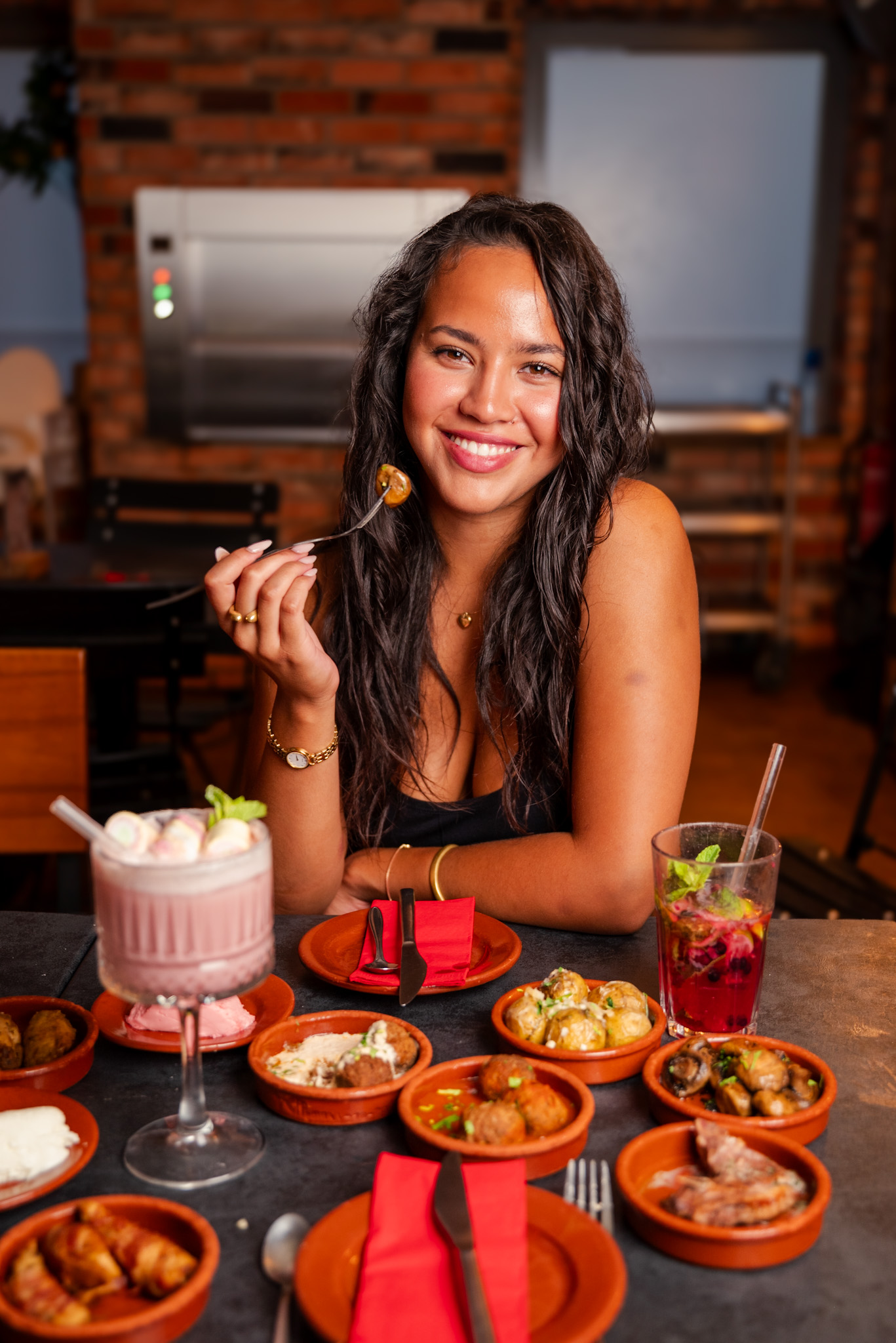 Frau sitzt lächelnd vor einer Auswahl an Tapas und zwei Cocktails im Tapas & More Dortmund