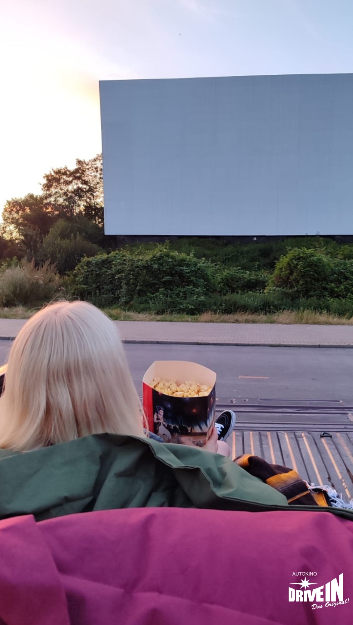 Frau mit Popcorn auf der Ladefläche eines Pick-ups beim Kinoabend im Autokino Essen