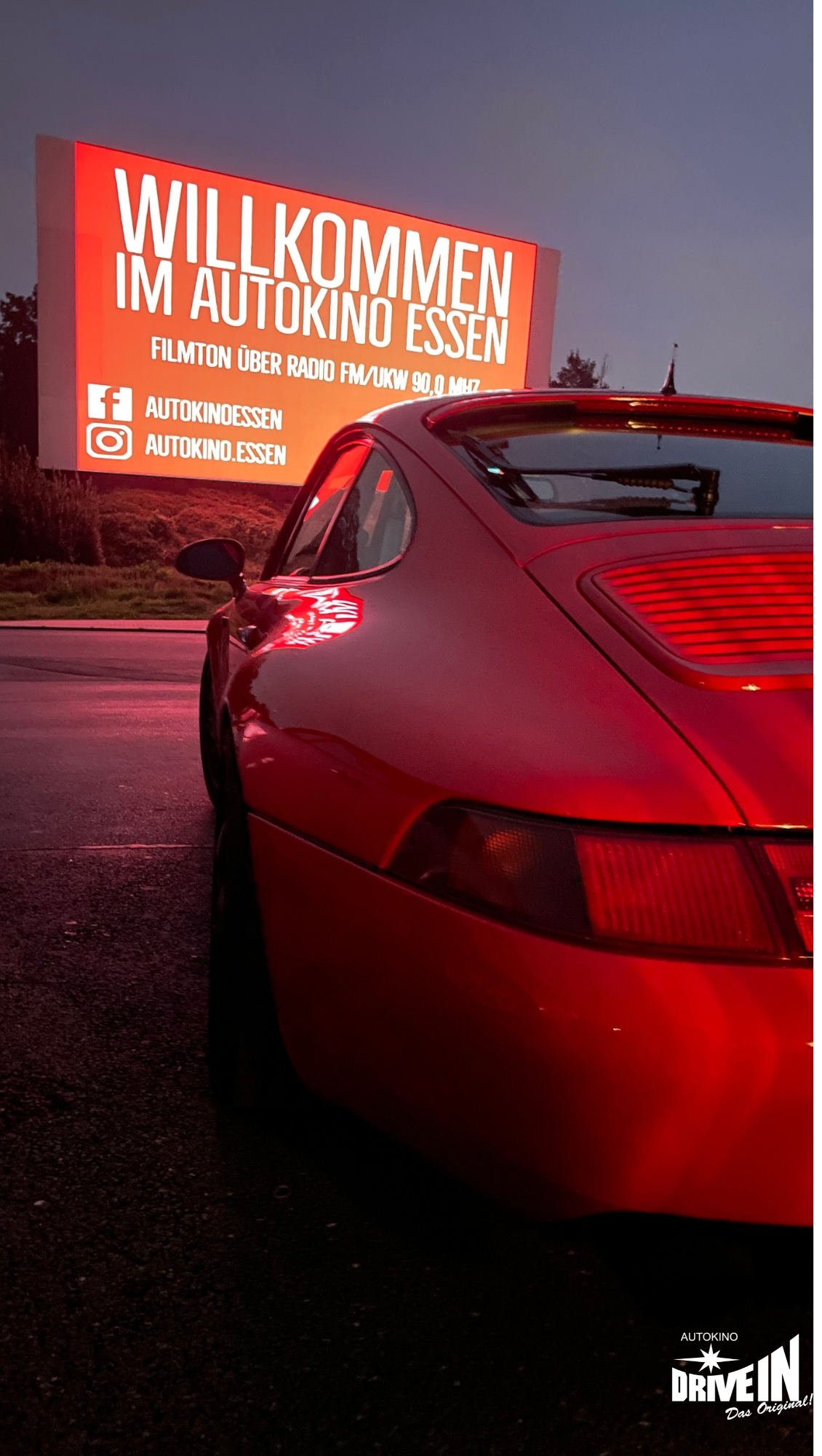 Roter Sportwagen vor beleuchtetem Willkommensschild im Autokino Essen bei Dämmerung