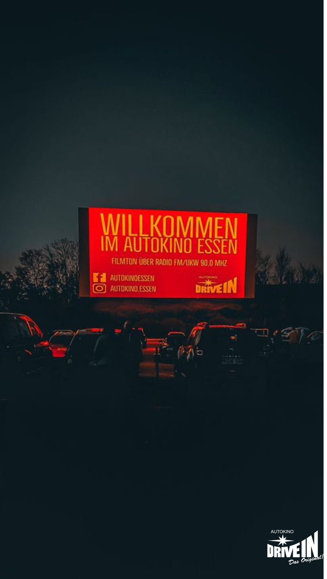 Rote Willkommensleinwand mit parkenden Autos im Autokino Essen bei Abendstimmung