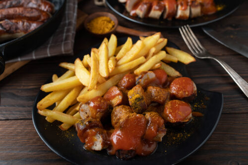 Currywurst mit Pommes und Currypulver auf einem Teller angerichtet