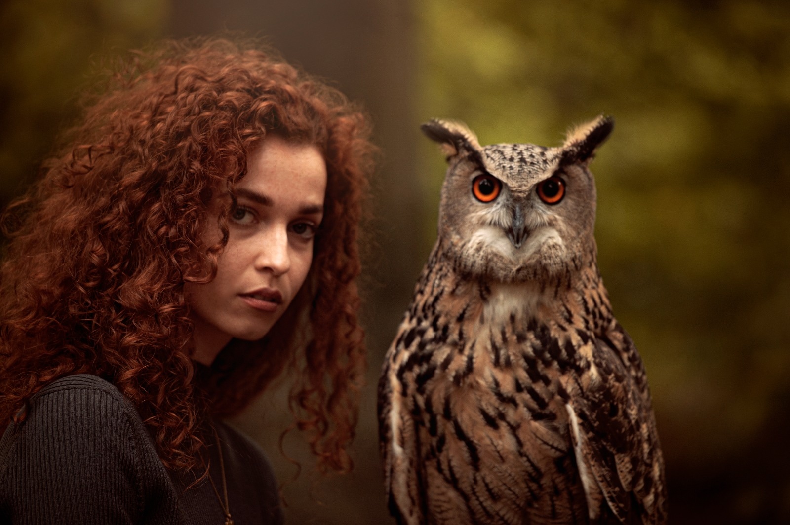 Junge Frau mit lockigem Haar und ein Uhu posieren gemeinsam für ein ausdrucksstarkes Portrait bei der Falknerei Skyhunters in Frechen