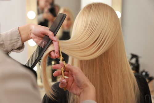 Friseurin schneidet sorgfältig lange blonde Haare mit Schere und Kamm im Salon