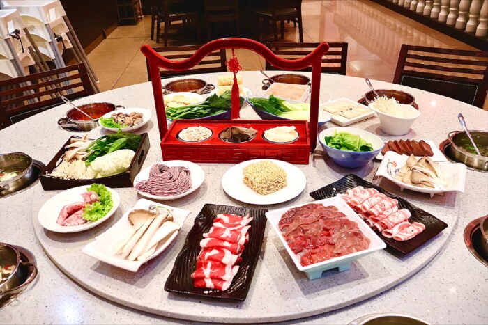 Reich gedeckter Tisch im Kylin Hotpot Dreieich mit frischen Zutaten wie Fleisch, Gemüse, Nudeln und Beilagen rund um ein traditionelles Serviergestell