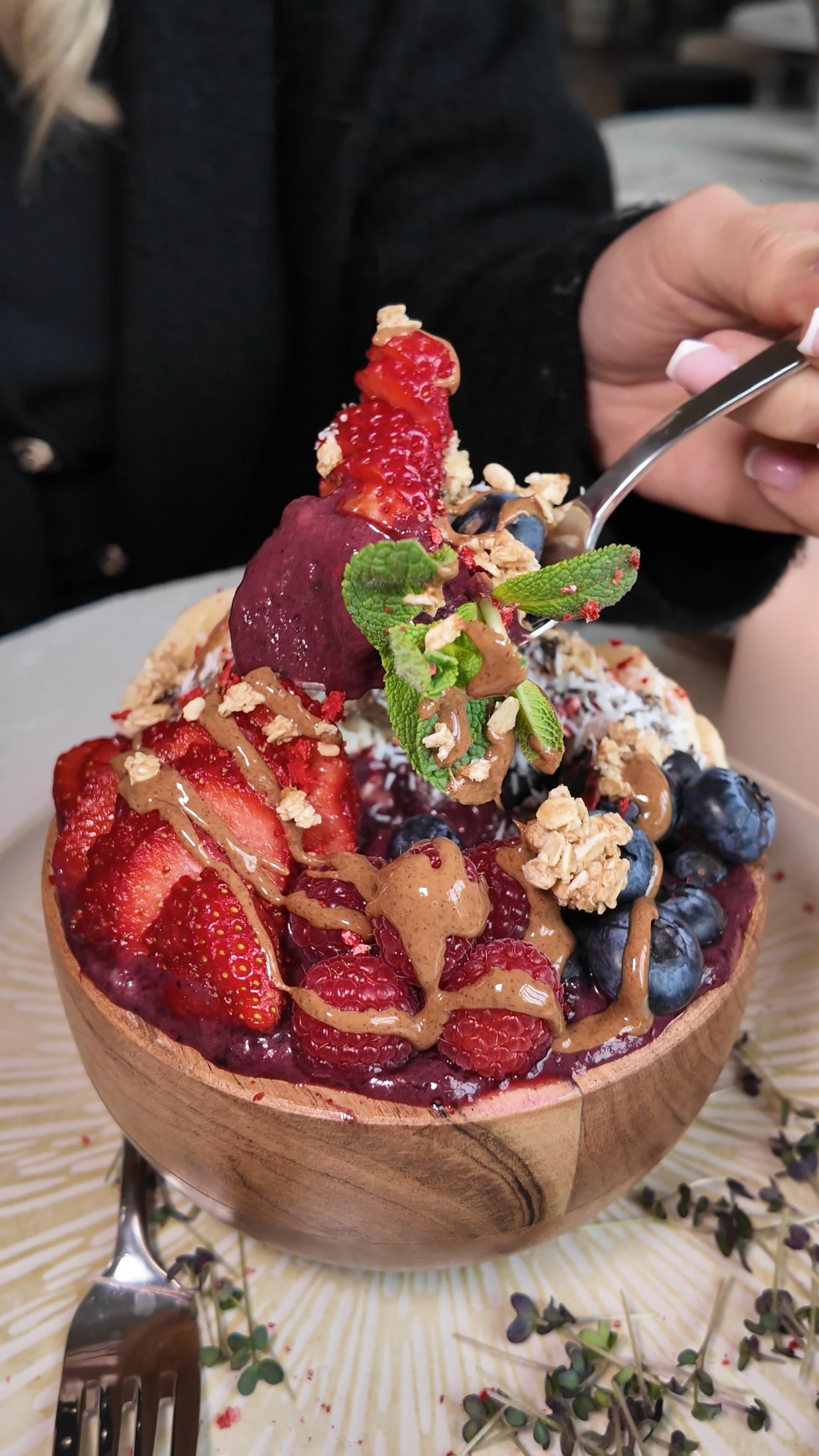 Acai-Bowl im LALA Smashburger Frankfurt mit frischen Erdbeeren, Blaubeeren, Granola, Minze, Erdnussbutter, Sorbet und Kokosflocken, angerichtet in einer Holzschale