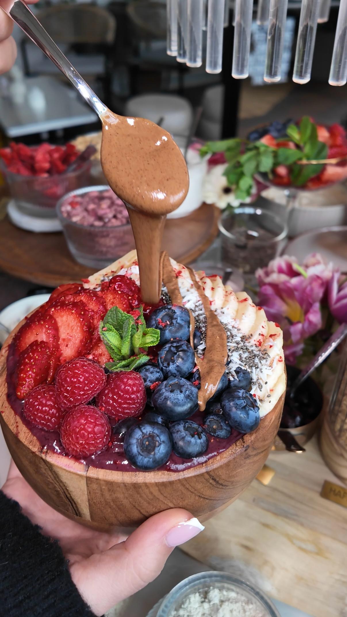 Acai-Bowl im LALA Smashburger Frankfurt mit Himbeeren, Blaubeeren, Erdbeeren, Kokosraspeln und Granola, garniert mit flüssiger Schokosauce und serviert in einer Kokosschale
