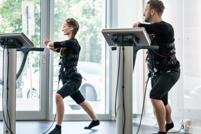 Mann und Frau beim Muskelaufbautraining mit EMS-Anzügen und elektronischer Steuerungseinheit