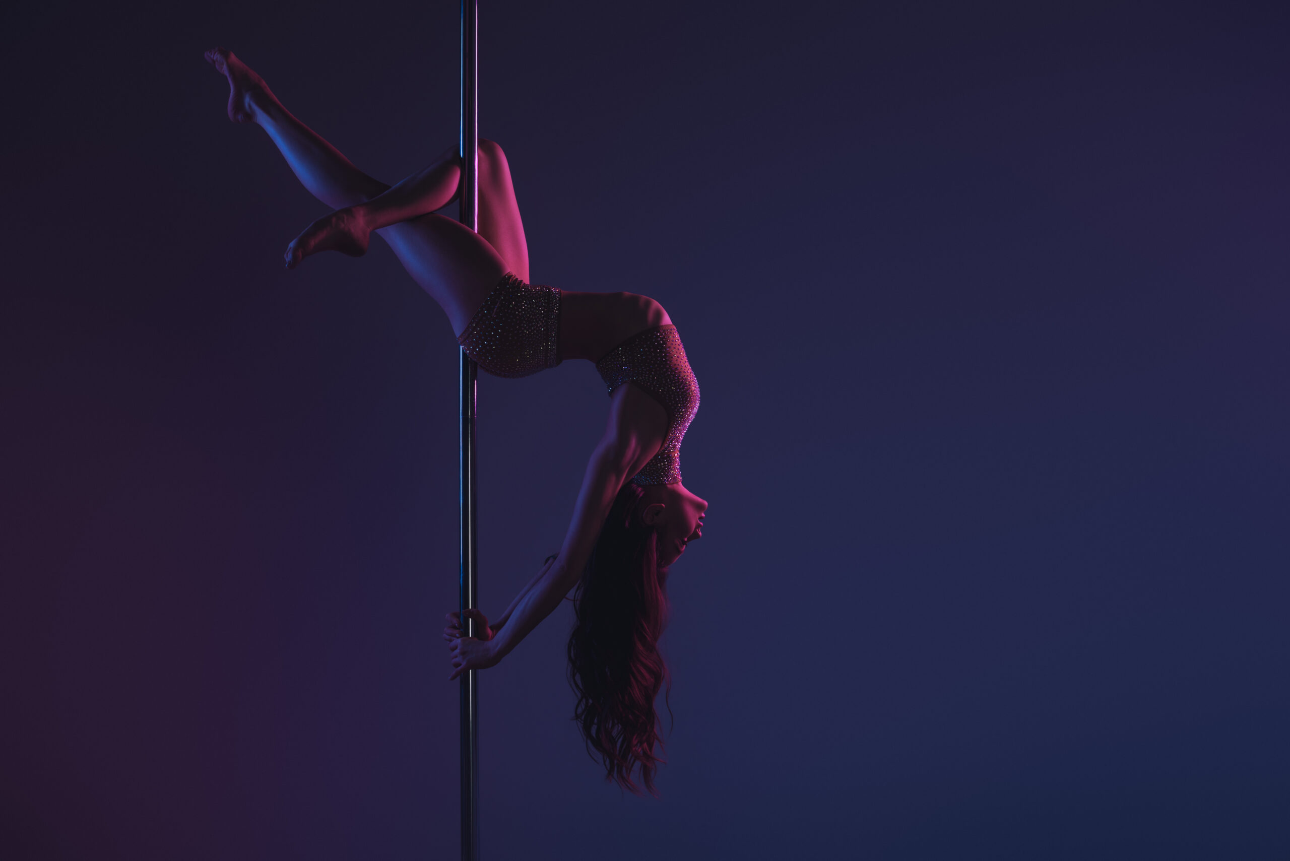 Frau beim Pole Dance in eleganter Pose unter dramatischer Bühnenbeleuchtung