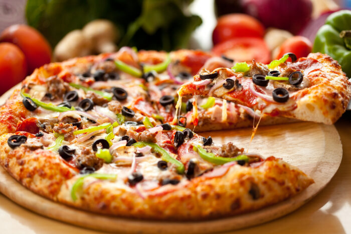 Frische Pizza mit Paprika, Oliven, Käse und weiteren Zutaten auf einem Holzbrett serviert