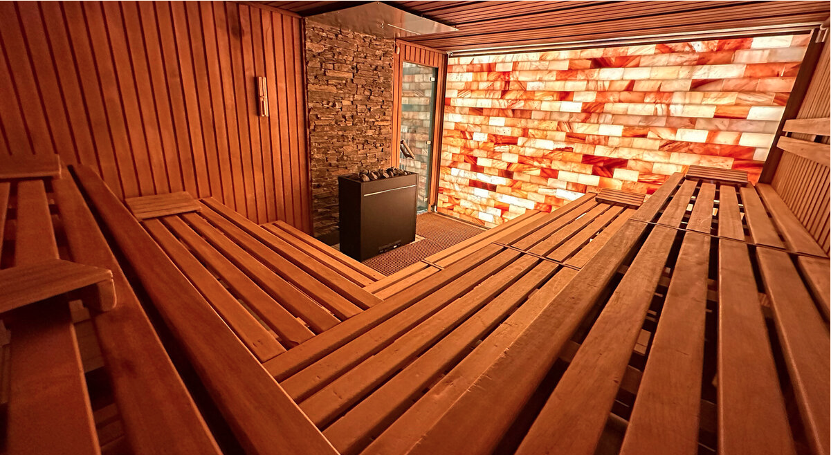 Stilvoll gestalteter Saunaraum mit Salzsteinwand, Holzbänken und Saunaofen in einem modernen Wellnessbereich