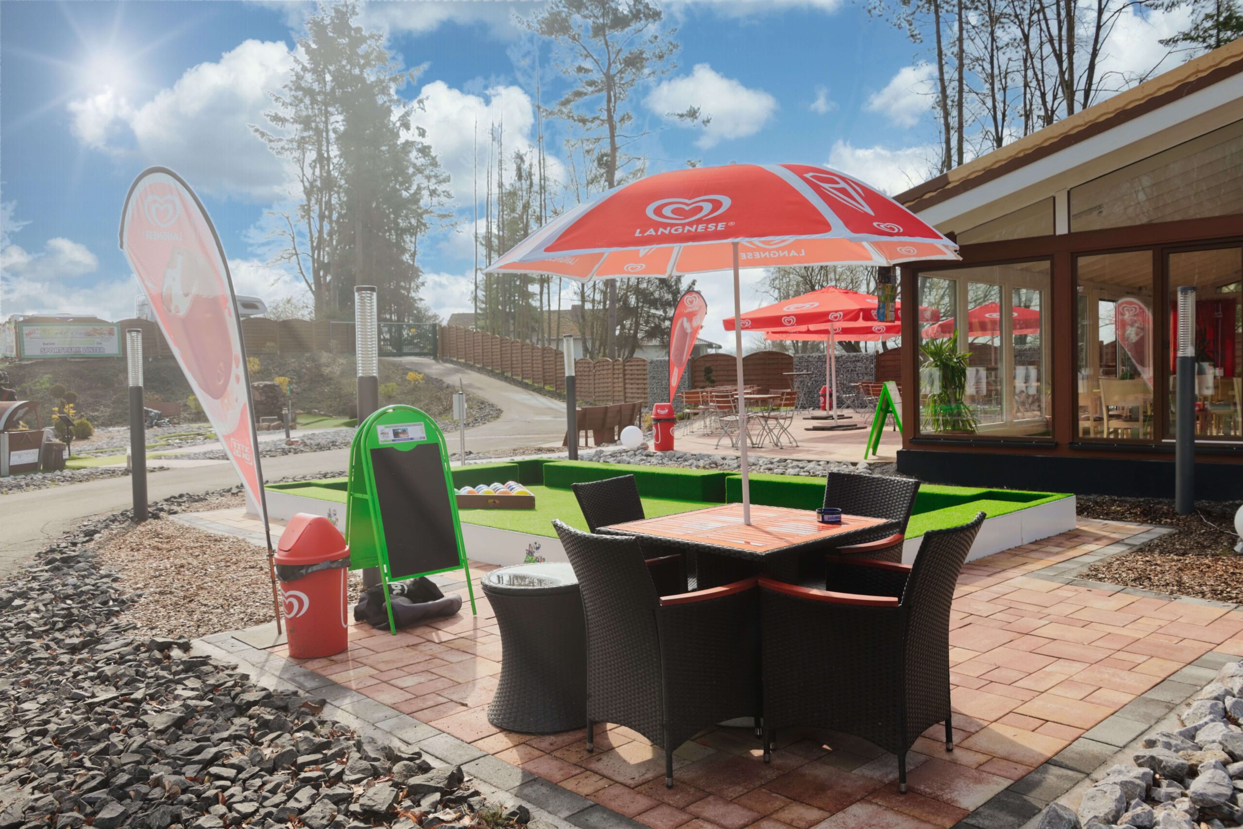 Gedeckter Sitzbereich mit Sonnenschirm im Außenbereich des Sport- und Freizeitparks Limburg-Linter, neben der Adventure Golf Anlage