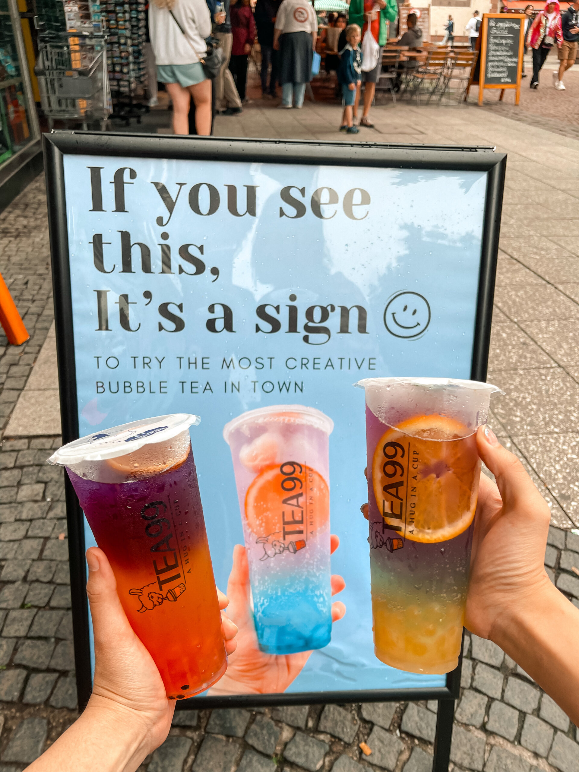 Drei bunte Bubble-Tea-Getränke von Tea99 Frankfurt vor einem Werbeschild mit der Aufschrift "If you see this, it’s a sign"