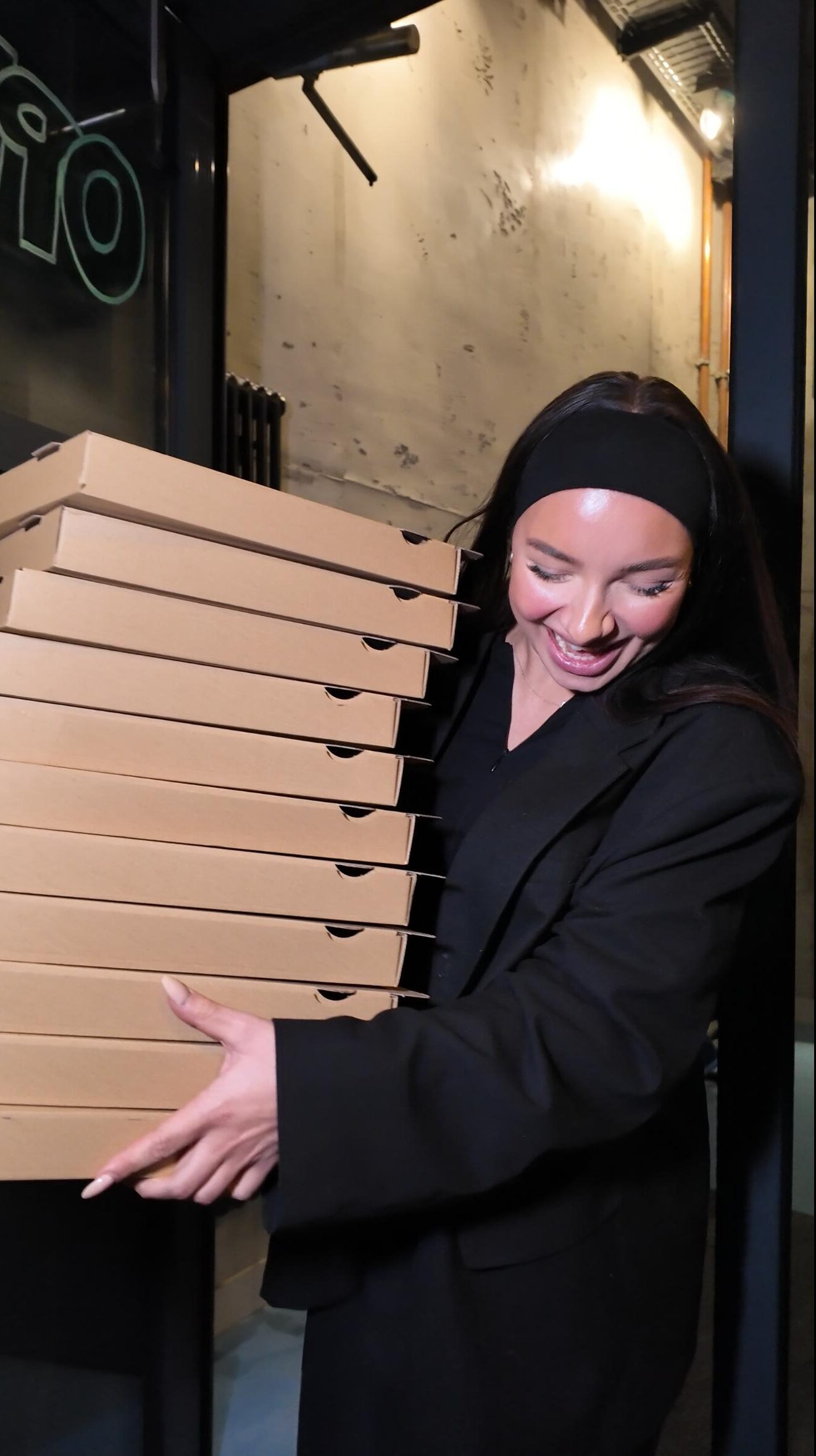 Eine lächelnde Frau trägt einen großen Stapel Pizza-Kartons für Abholung bei Zampano To Go in Frankfurt