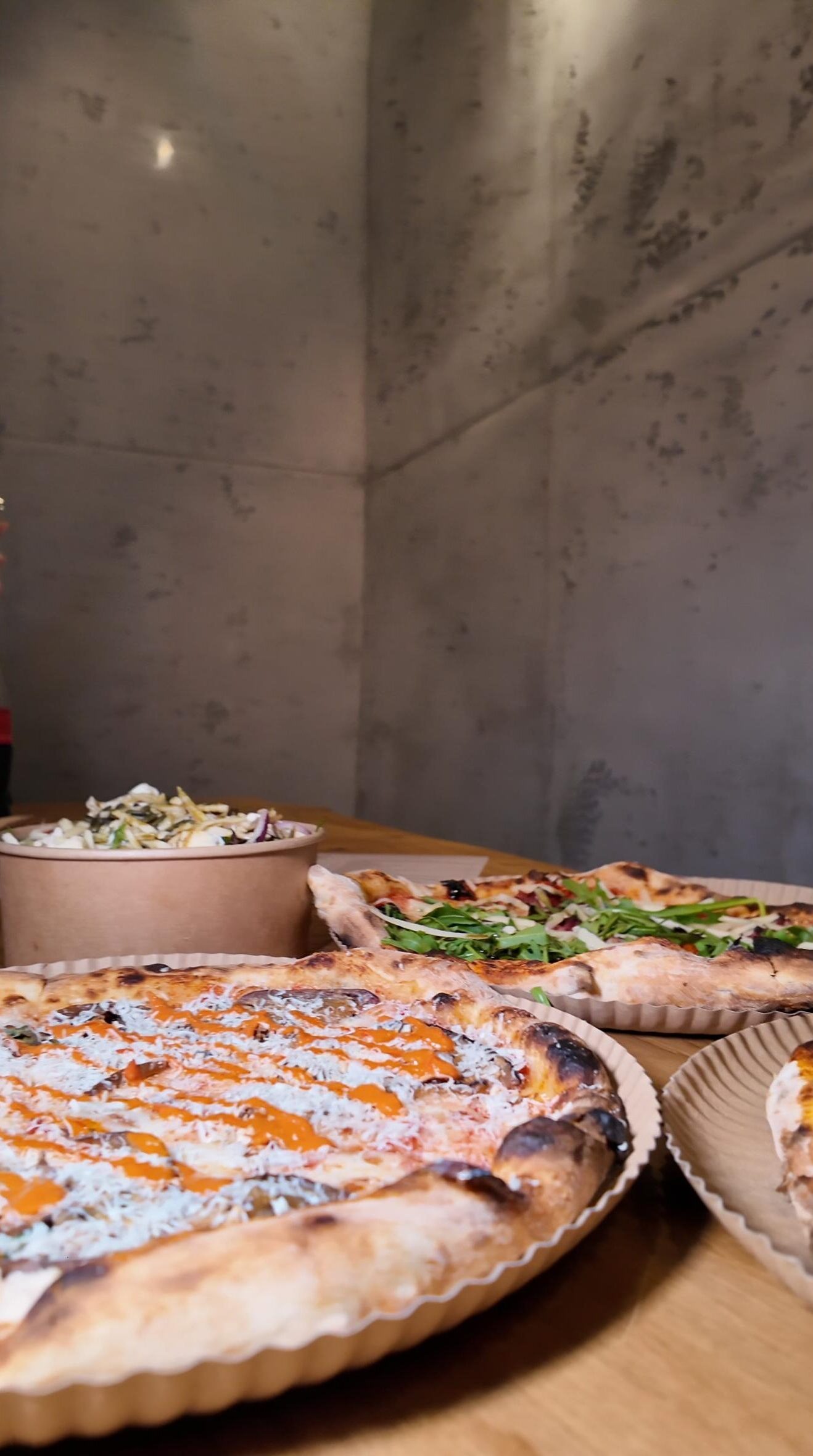 Pizza mit knusprigem Rand, frischem Rucola, cremiger Sauce sowie frischer Salat im Hintergrund bei Zampano To Go Frankfurt