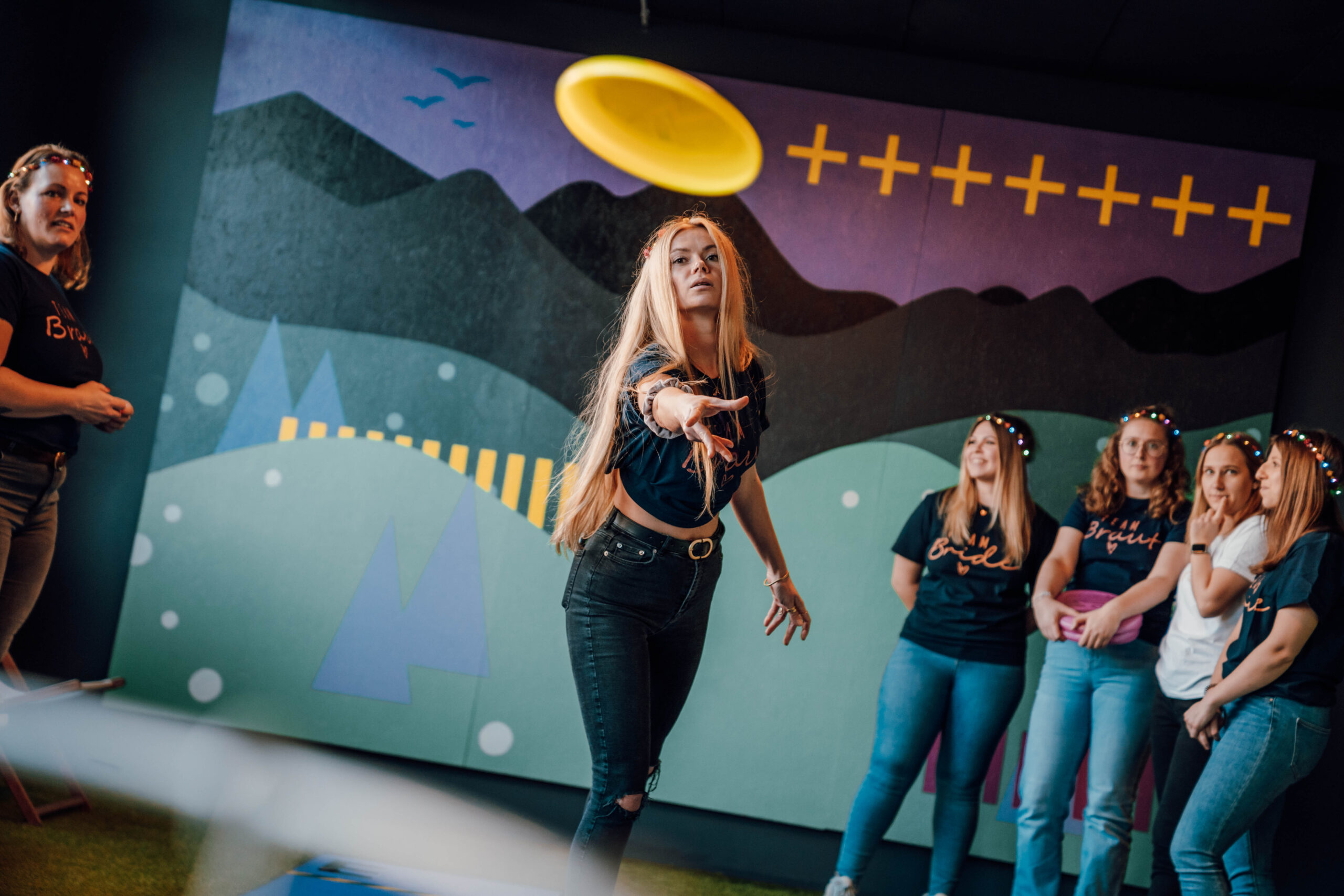 Junge Frau wirft eine gelbe Frisbee in einer Indoor-Spielarena der Face Off GmbH Rüsselsheim, während andere Teilnehmer zusehen