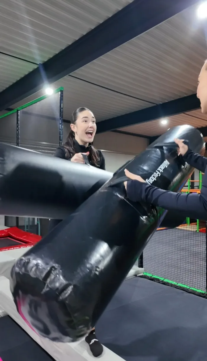 Zwei Frauen stehen sich in der Duell-Arena von FunFusion Wetzlar gegenüber und kämpfen mit gepolsterten Stäben auf einer Schaumstoffplattform – Spaß und Action garantiert