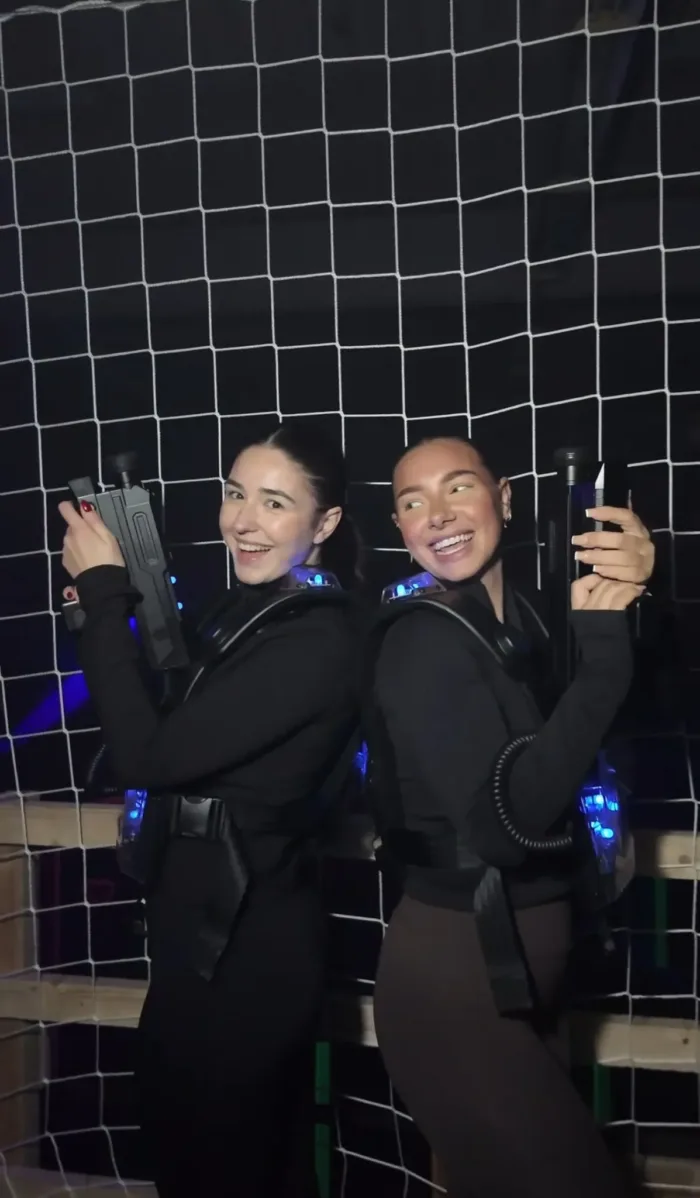Zwei Spieler mit Lasertag-Westen und Phasern posieren Rücken an Rücken vor einem Netz in der Lasertag-Arena von FunFusion Wetzlar – mit blauen Leuchteffekten