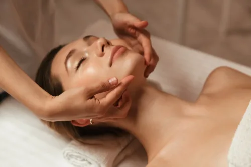 Frau liegt entspannt auf einer Behandlungsliege und erhält eine sanfte Gesichtsmassage