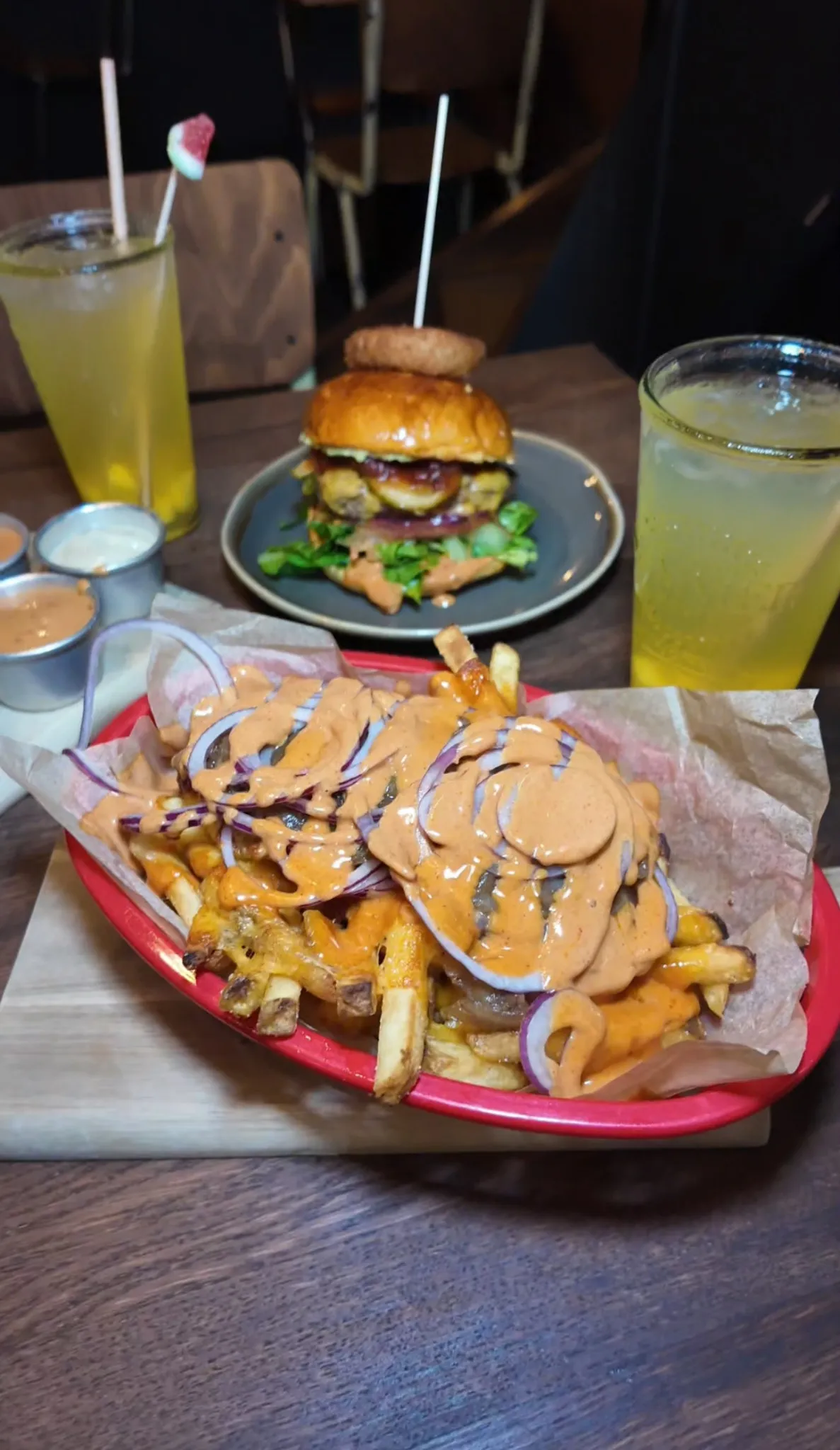 Beladene Pommes mit Saucen und roten Zwiebeln in roter Schale, dazu ein Burger mit Salat und zwei Gläser Zitronenlimonade im Hornochse Köln