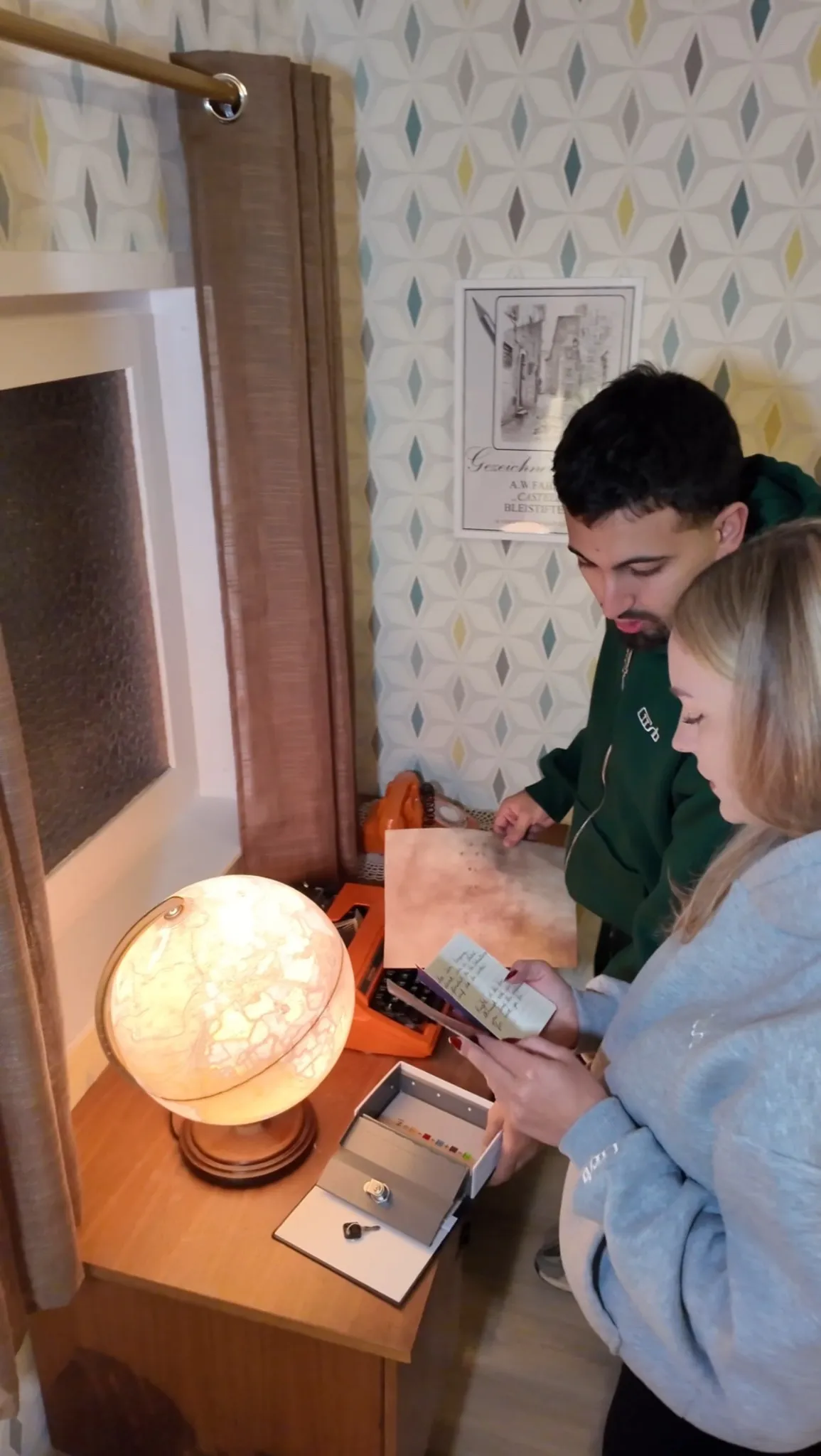 Zwei Personen rätseln im Escape Room „Muriel_Ingrid“ an einem Schreibtisch mit Globuslampe, Schreibmaschine und Karte