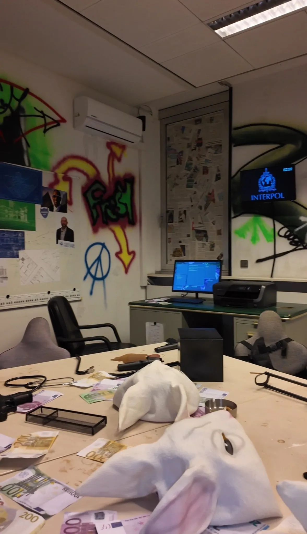 Ansicht eines Escape Rooms im Hacker-Stil bei Face Off Rüsselsheim mit Graffitis an der Wand, Computern, Kabeln, Masken und Chaos auf dem Tisch