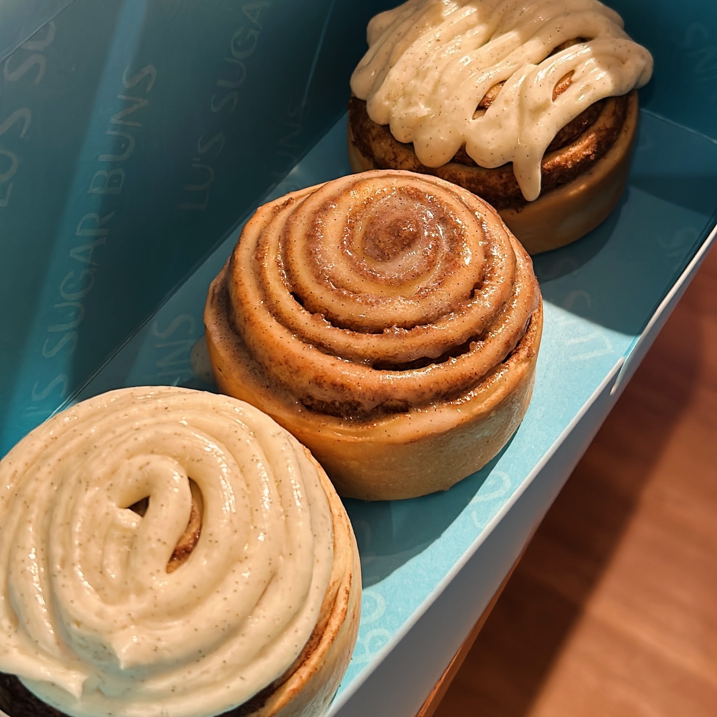 Drei frische Zimtschnecken in einer türkisfarbenen Box von LU’s Sugar Buns Hanau, teils pur, teils mit cremigem Frosting garniert