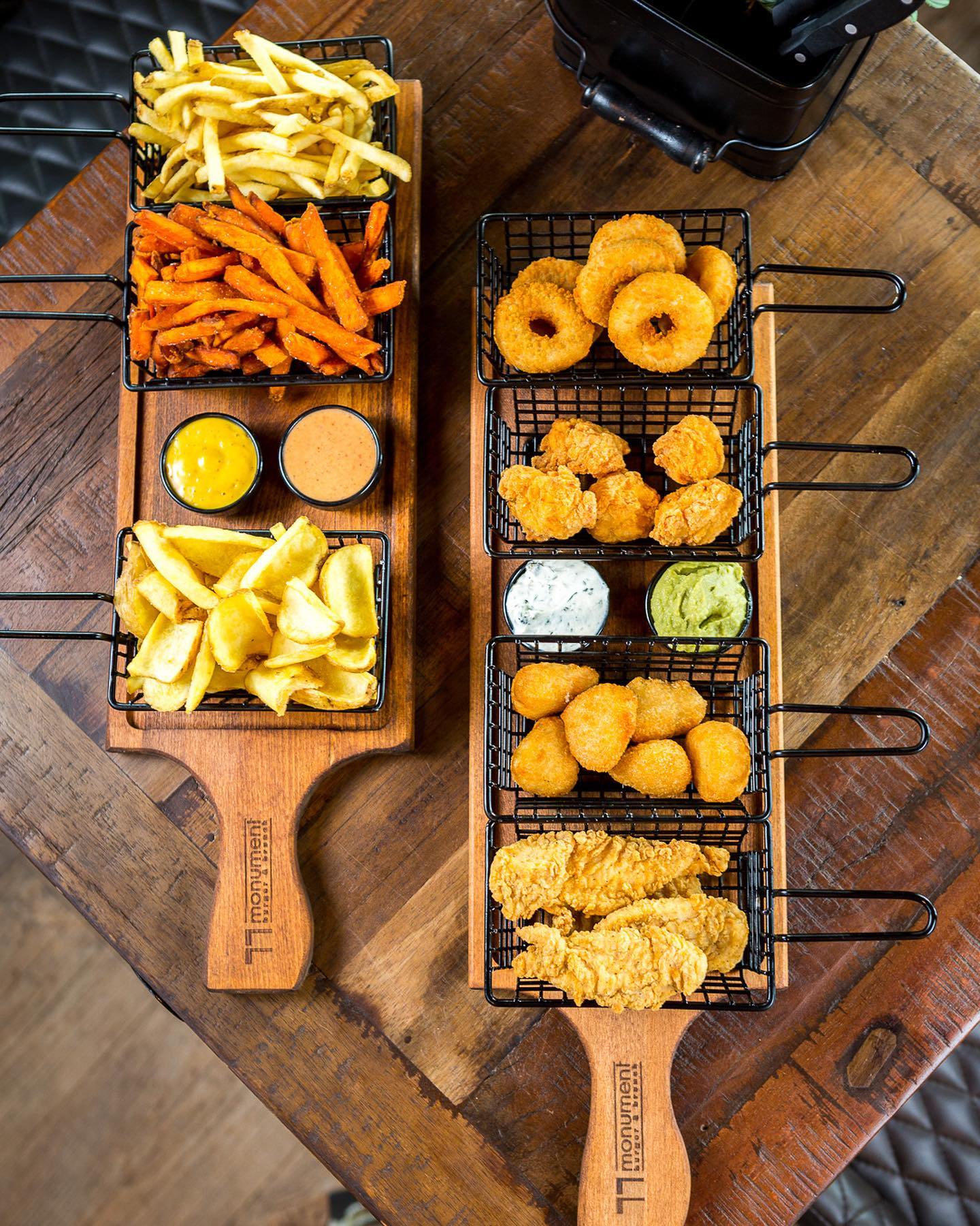 Zwei große Servierbretter im Monument Burger Leverkusen mit Pommes, Süßkartoffelpommes, Onion Rings, Nuggets, Chicken Strips und verschiedenen Dips in Metallkörben angerichtet
