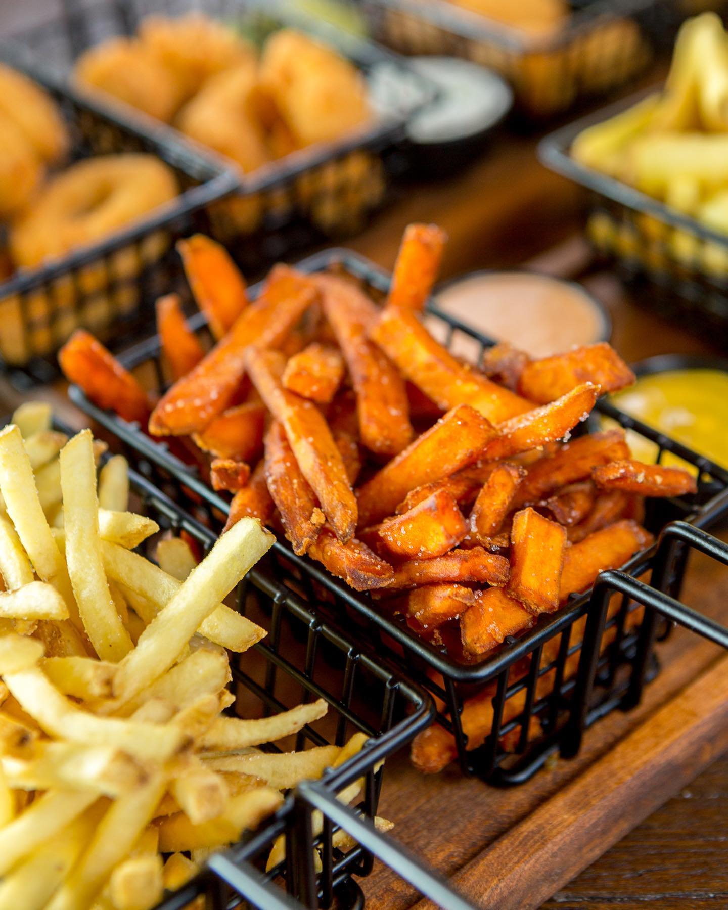 Süßkartoffelpommes und klassische Pommes in kleinen schwarzen Metallkörbchen, serviert mit Dips im Monument Burger Leverkusen