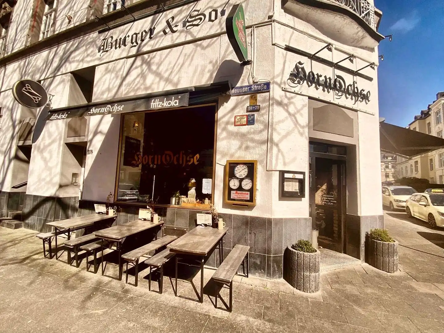 Außenansicht des Hornochse Köln bei Sonnenschein mit Tischen vor dem Lokal, markanter Fassadenbeschriftung und rustikalem Eingang