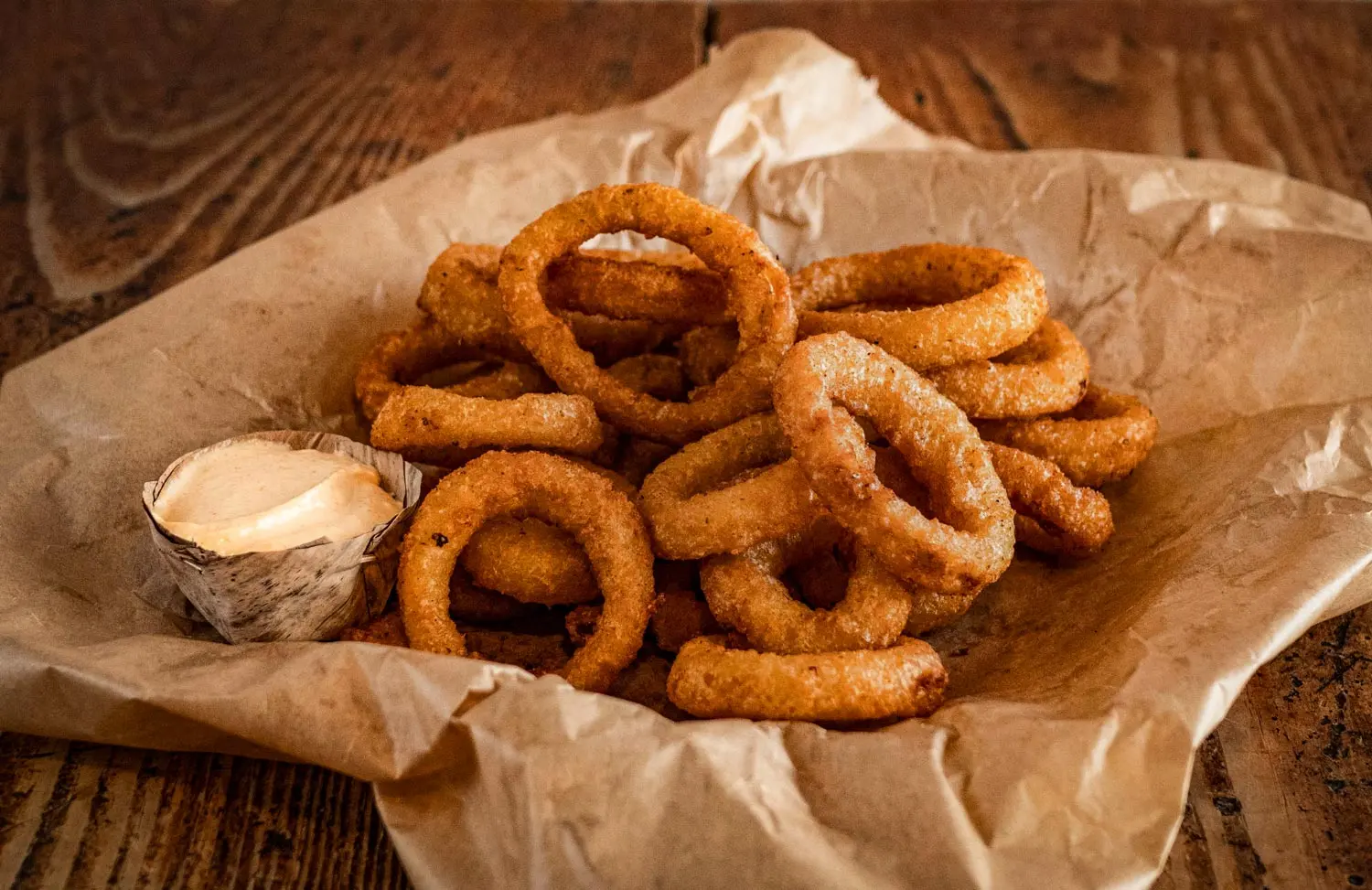 Knusprige Onion Rings vom Red Barn BBQ Restaurant auf Backpapier serviert, dazu ein cremiger Dip auf rustikalem Holztisch