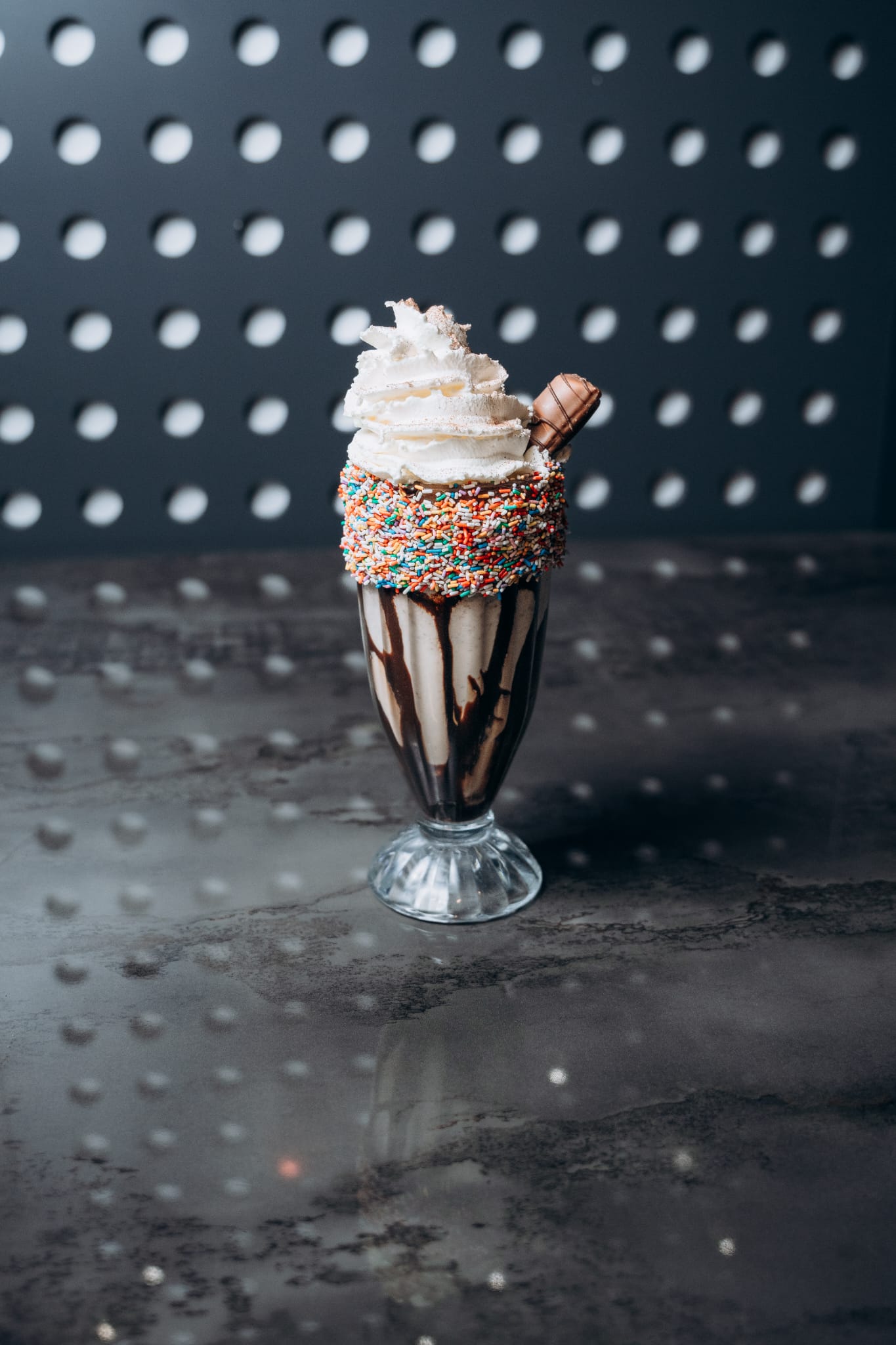 Spektakulärer Deluxe-Milchshake im hohen Glas mit Schokosauce, Sahnehaube, Waffelröllchen und bunten Streuseln am Glasrand – serviert bei Shiva Food and More Dinslaken