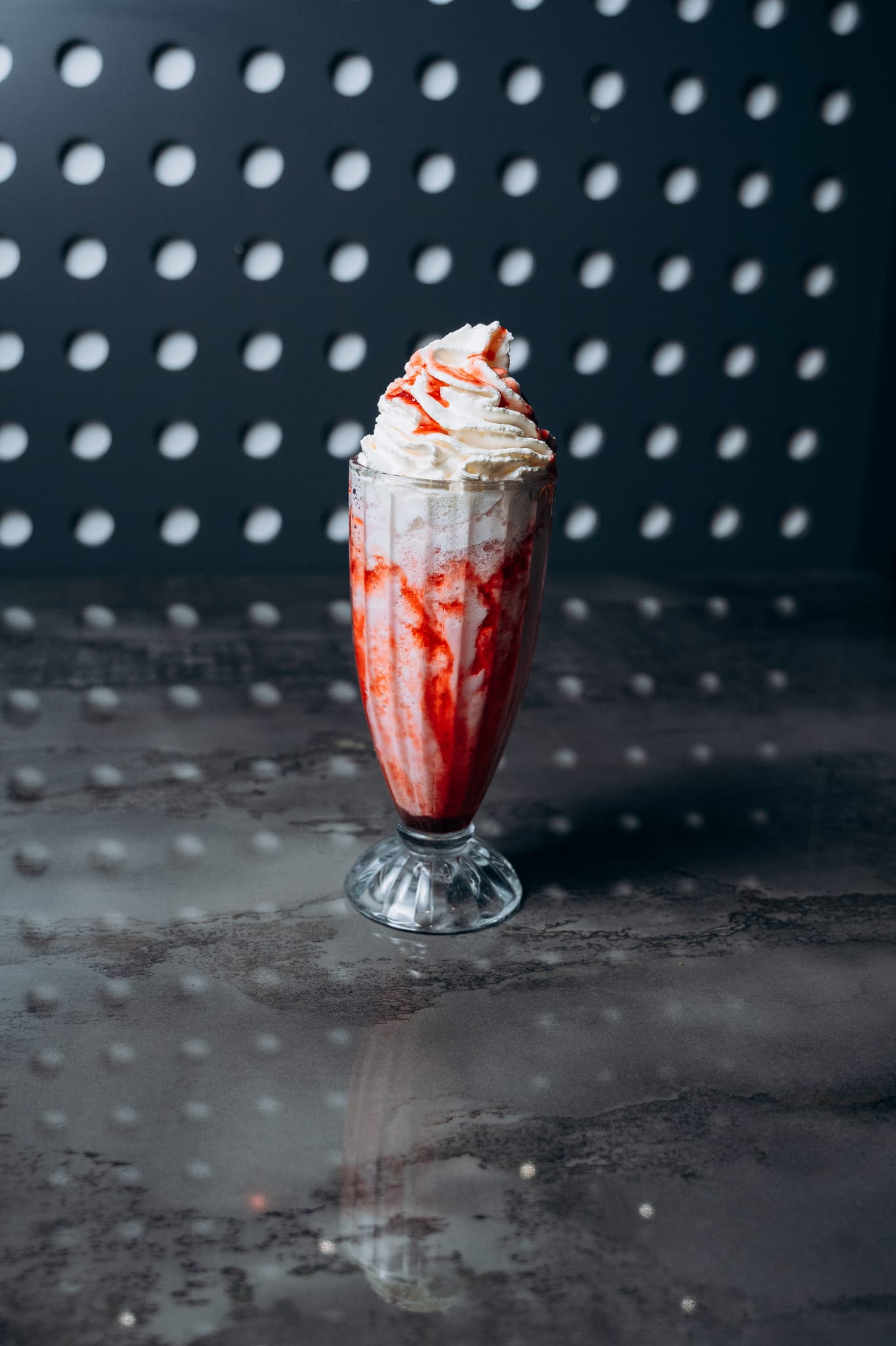 Hoher Erdbeer-Milchshake im Glas, garniert mit Sahnehaube und Erdbeersauce, serviert im modernen Interior von Shiva Food and More Dinslaken
