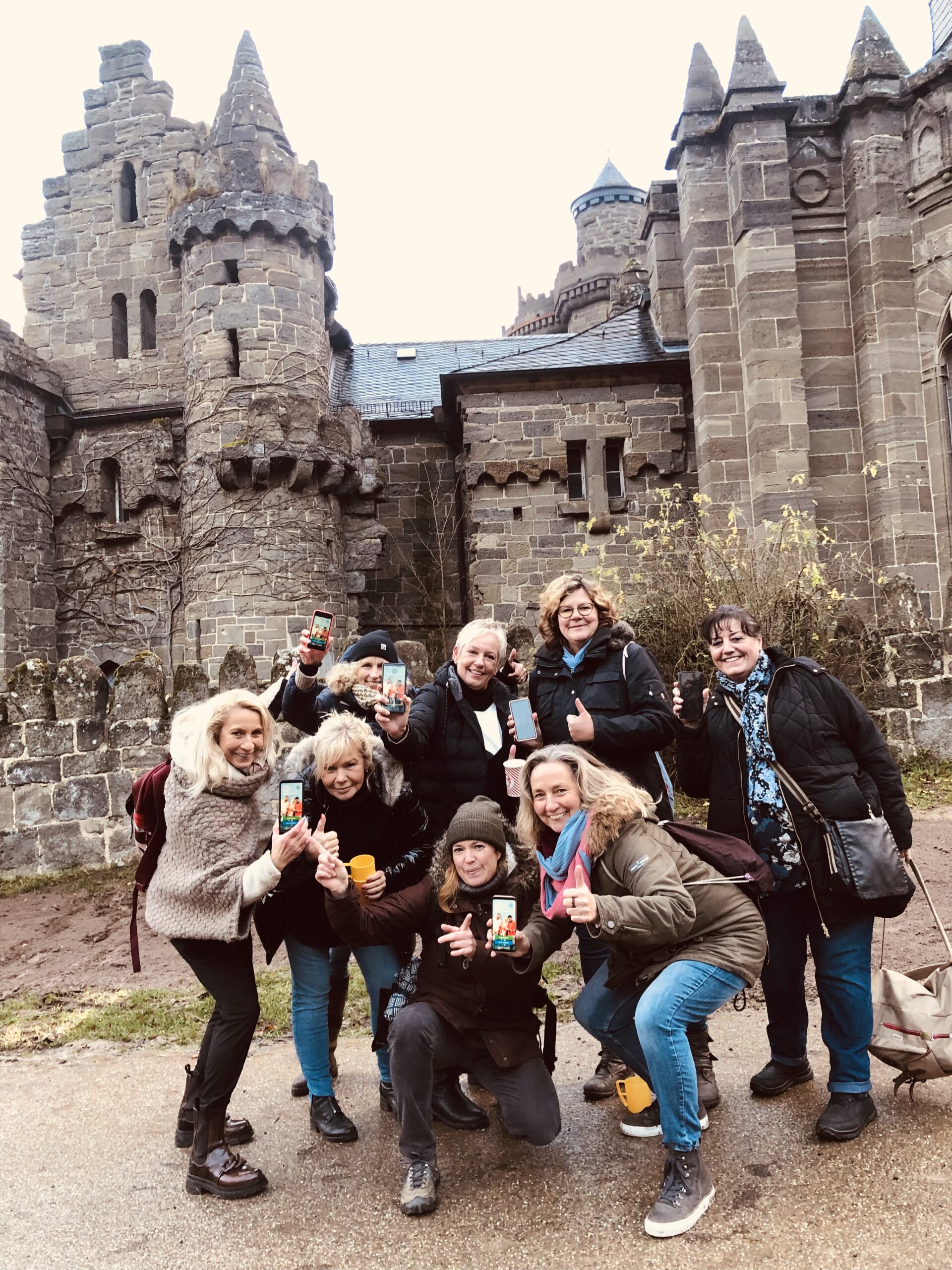 Stadtkrimi-Gruppe posiert lachend vor der Löwenburg in Kassel, gut gelaunt und wetterfest gekleidet – gemeinsames Krimiabenteuer im Team