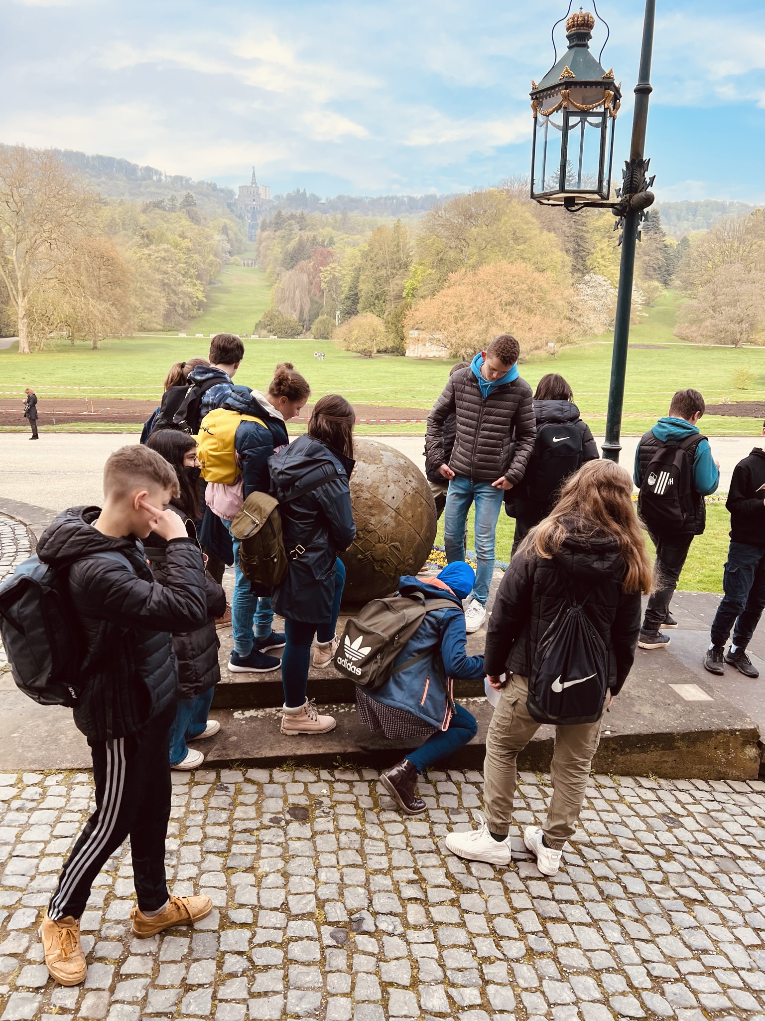 Gruppe von Jugendlichen, vermutlich eine Schulklasse, löst ein Rätsel bei den Stadtkrimis Kassel im Freien, mit Blick über eine Parkanlage und herbstliche Landschaft