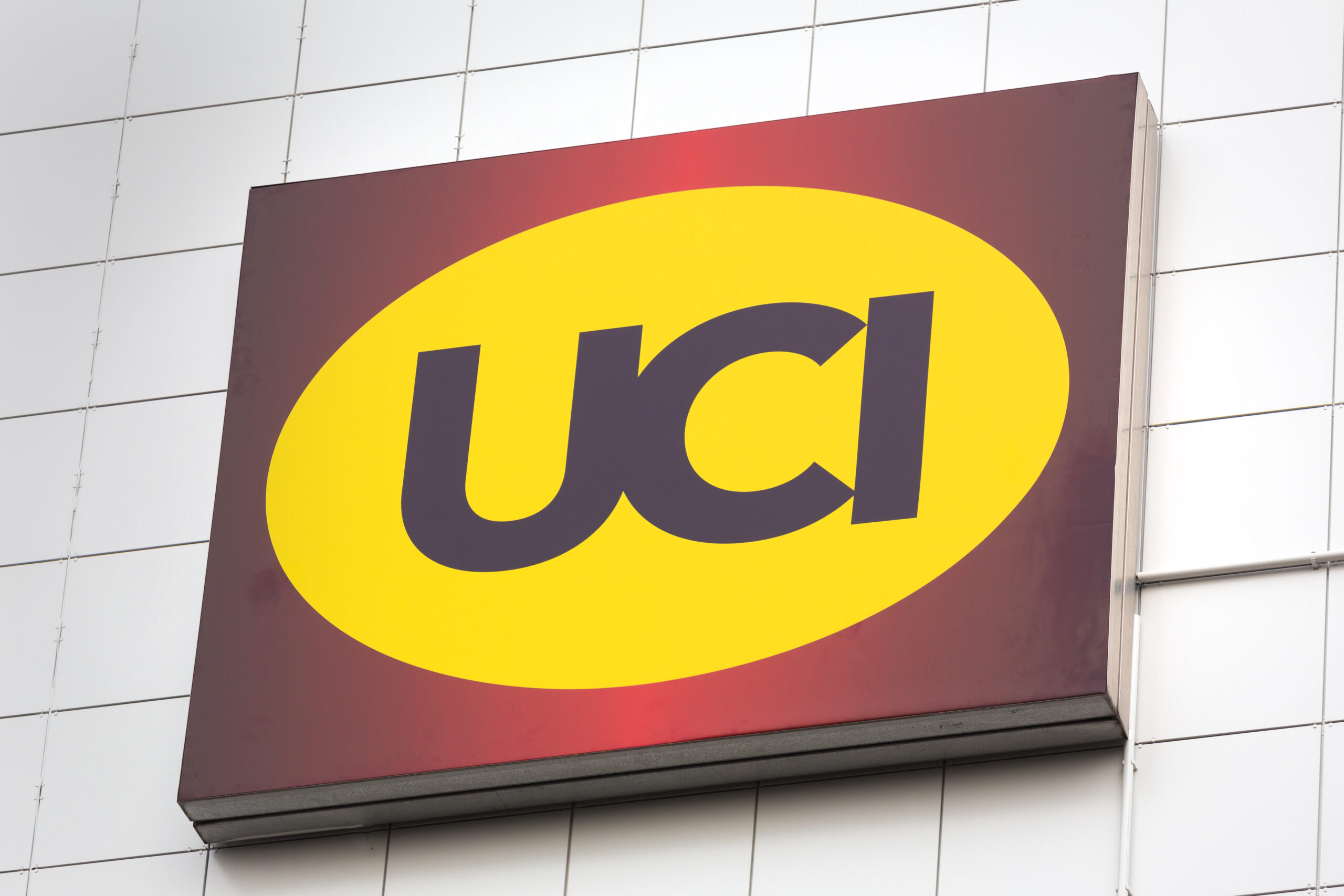 UCI Kinowelt Logo in gelbem Oval auf rotem Hintergrund, angebracht an einer hellen Gebäudeaußenfassade