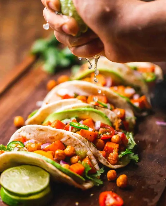 Hand presst Limette über vegane Tacos mit Kichererbsen, Paprika und Salat