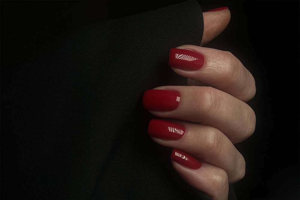 Hand mit klassisch rot lackierten Fingernägeln vor schwarzem Hintergrund