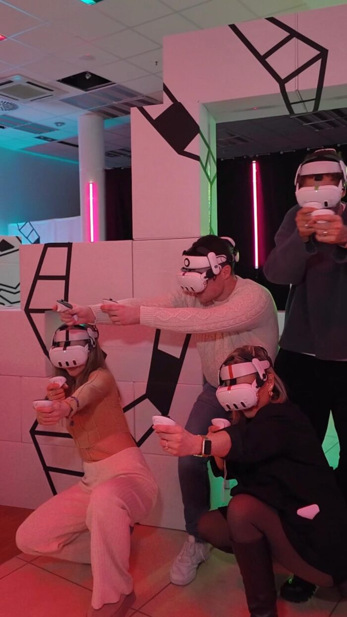 Gruppe von vier Personen spielt gemeinsam VR-Laser-Tag hinter Deckung in einer stylischen Arena in Berlin.