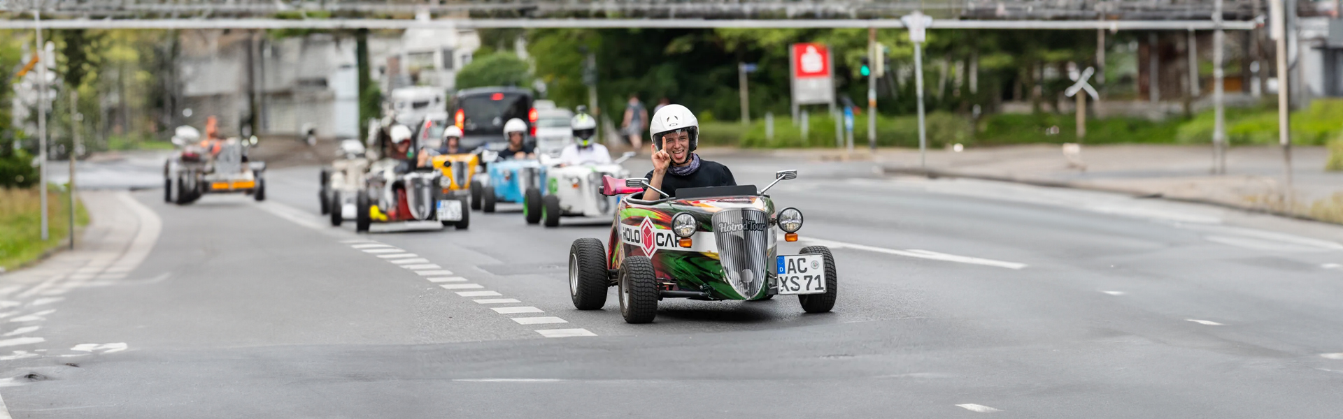 Teilnehmer einer Hotrod-Tour fährt im Mini-Fahrzeug mit Helm durch die Innenstadt von Aachen