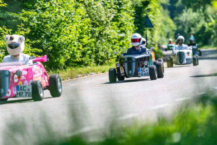 Teilnehmer der Hotrod Tour Aachen fahren mit Mini-Hotrods auf einer Landstraße bei sonnigem Wetter durch grüne Umgebung