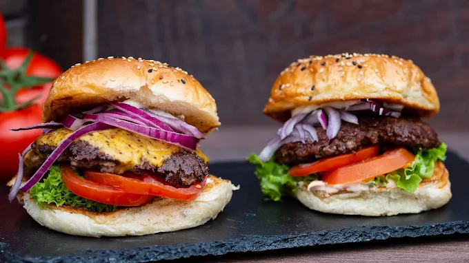 Zwei saftige Burger mit Cheddar, Tomate, Salat und roten Zwiebeln auf schwarzem Schiefer
