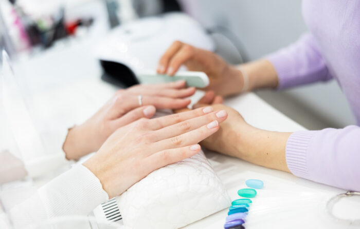 Professionelle Maniküre mit Feile im Nagelstudio, Farbpalette im Vordergrund