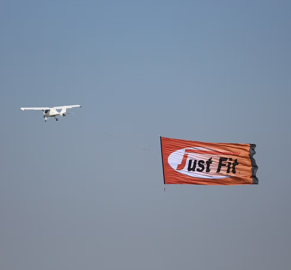 Flugzeug zieht ein Werbebanner mit der Aufschrift "Just Fit" über den Himmel, aufgenommen bei klarem Wetter durch Profievents Sankt Augustin