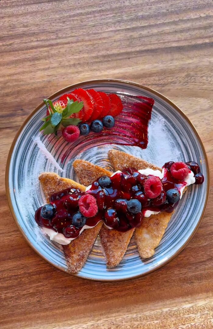 Dessert mit frischen Beeren, Sahne und Fruchtsauce auf einem dekorativen Teller