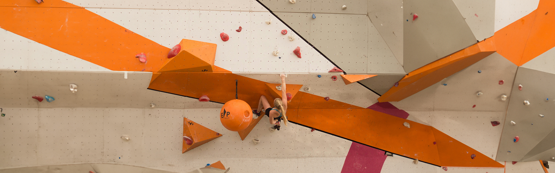 Kletterer an einer orangen Boulderwand mit verschiedenen Griffen im Sportpoint Meckenheim