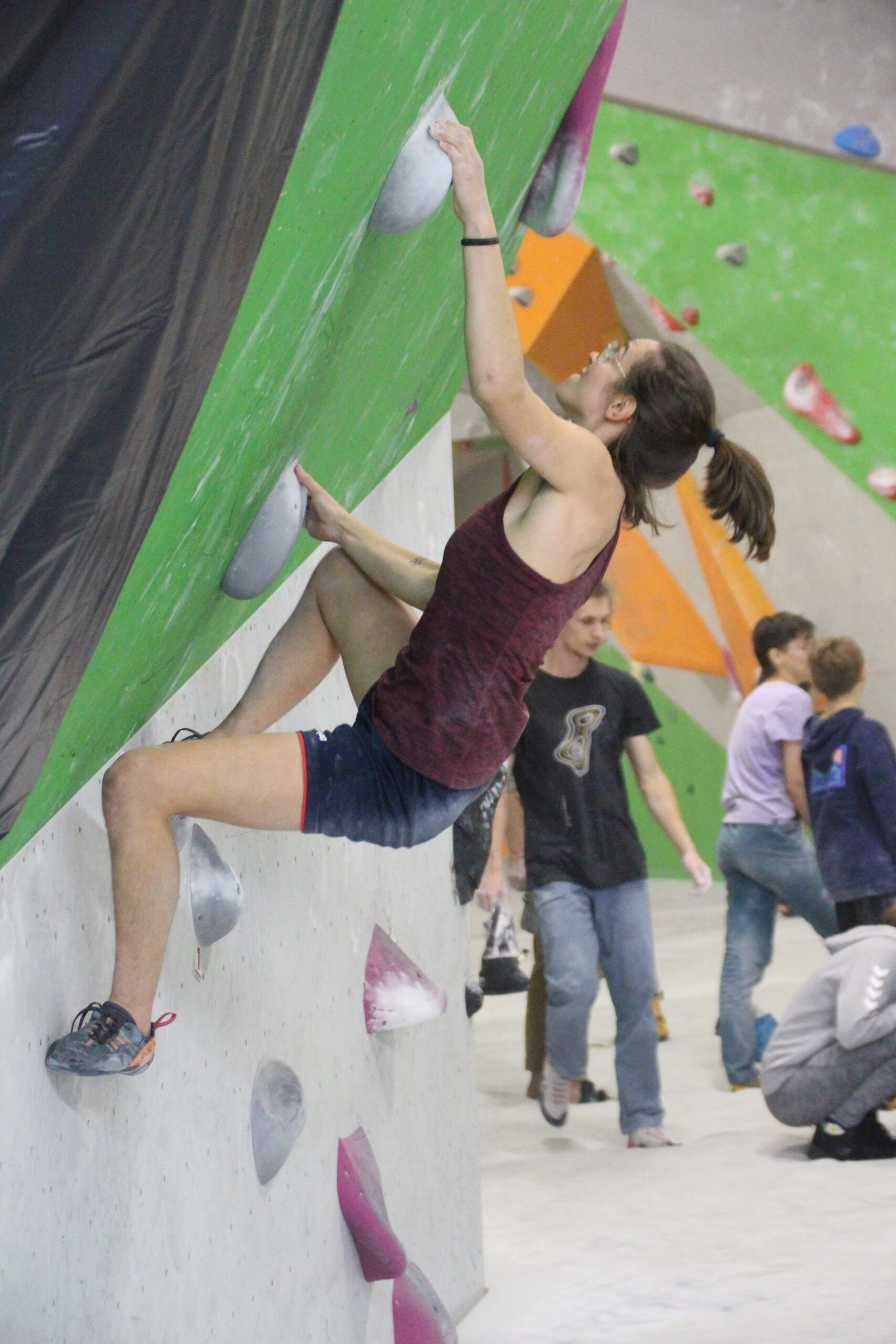 Junge Frau beim Bouldern an einer Kletterwand in einer Indoorhalle